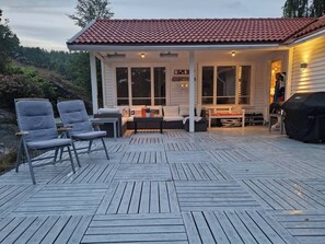 A covered outdoor deck with seating and a barbecue grill.