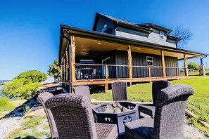 A modern house with a covered patio area, outdoor seating, and a view of the ocean. - Game day convenience and lakeside fun with is cute waterfront house (Graford)