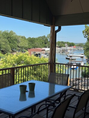 A covered outdoor seating area with a table and chairs, overlooking a body of water with docks and boats. - Game day convenience and lakeside fun with is cute waterfront house (Graford)