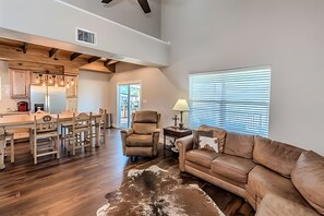 A spacious living area with a leather couch, wooden dining table, and a cowhide rug. - Game day convenience and lakeside fun with is cute waterfront house (Graford)