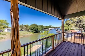 Une terrasse en bois avec une balustrade donnant sur une rivière et un espace vert avec des arbres et des bateaux.