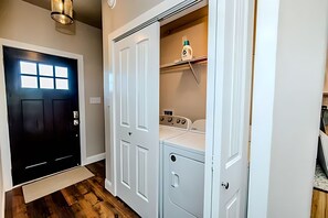 A laundry room with a washing machine, dryer, and a shelf with a bottle. - Game day convenience and lakeside fun with is cute waterfront house (Graford)