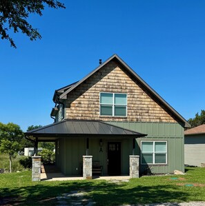 A two-story house with a gabled roof, a front porch, and a stone pillar. - Game day convenience and lakeside fun with is cute waterfront house (Graford)