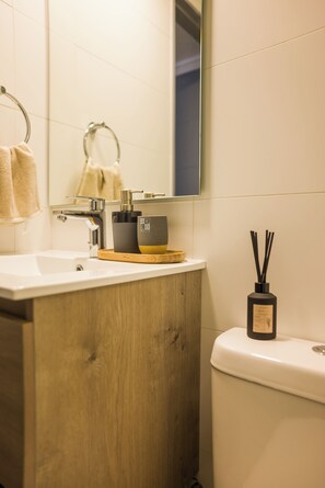 Ein Badezimmer mit einem Holzwaschtisch, einem weißen Waschbecken, einem Spiegel, einem Handtuchhalter, einer Toilette und einer Flasche mit Reisediffusor.