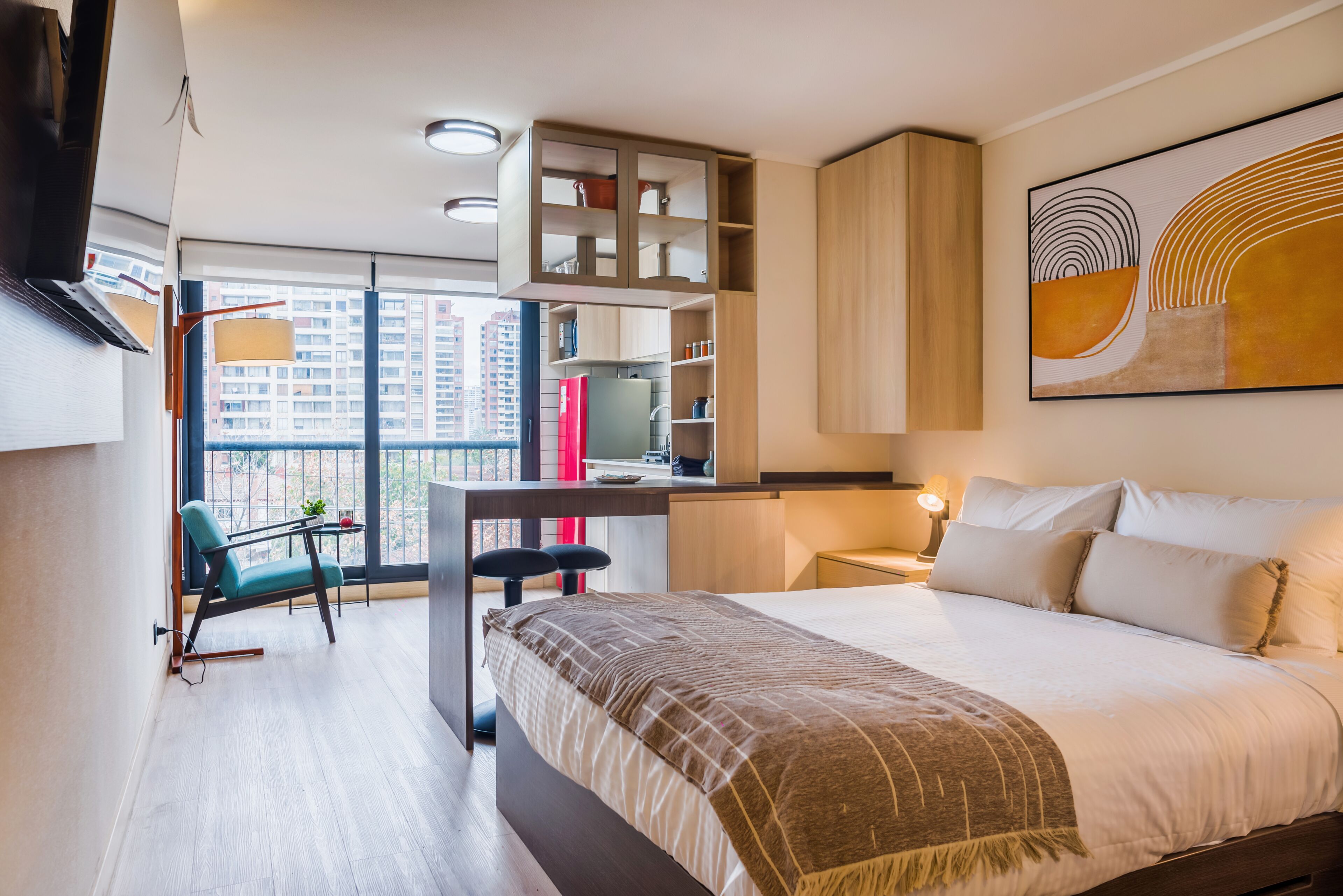 A modern hotel room with a bed, a desk, and a view of the city through large windows.
