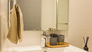 Ein Badezimmer mit einem weißen Waschbecken, einem Handtuch an einem Haken, einem Spiegel und einer kleinen Holztablett mit zwei Tassen.