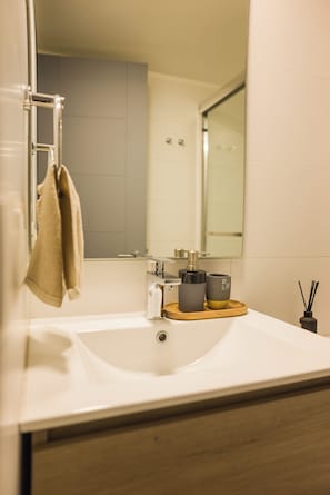 Ein Badezimmer mit einem weißen Waschbecken, einem Handtuch an einem Haken, einem Spiegel und einer kleinen Holztablett mit zwei Tassen.