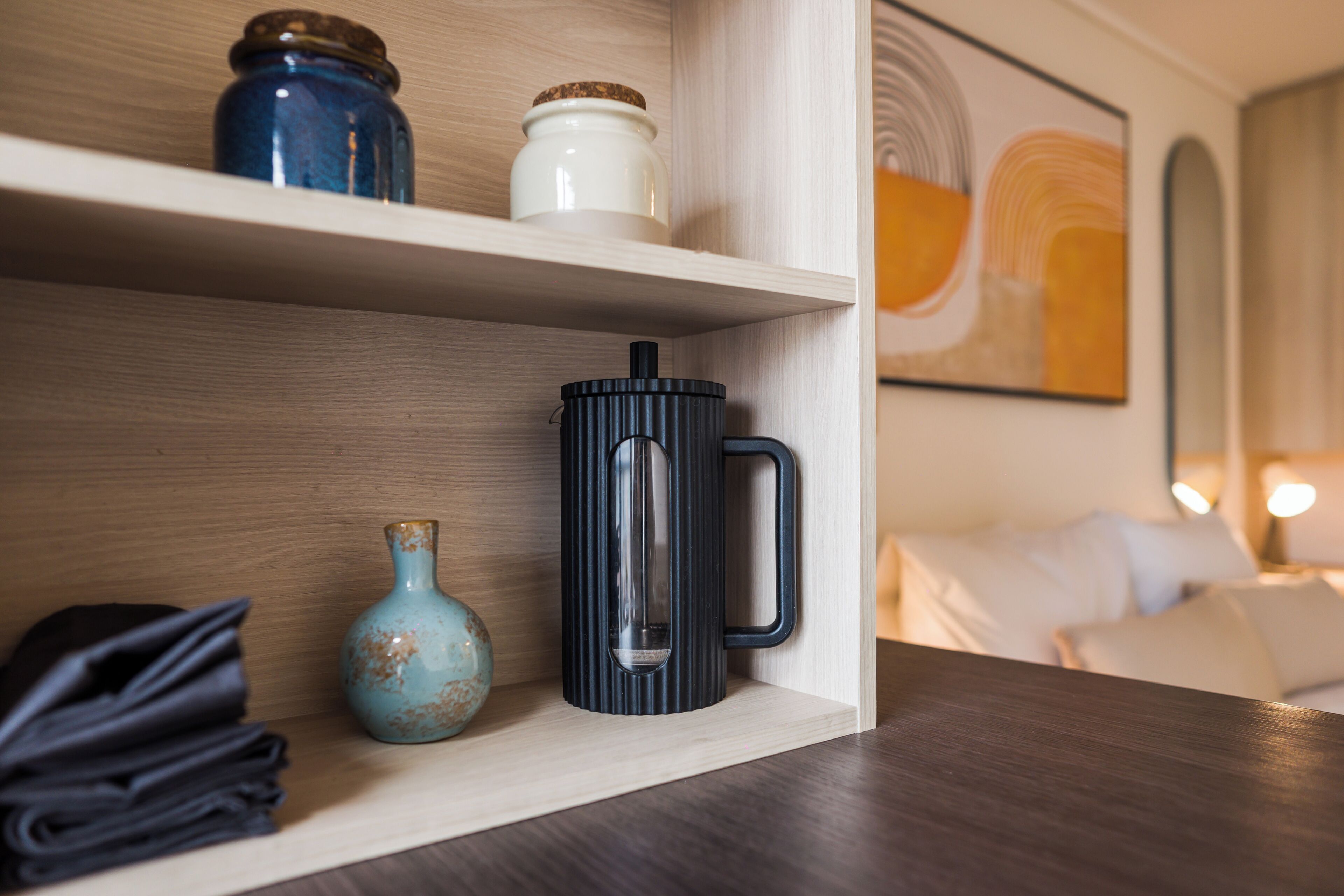A shelf with a black mug, a blue vase, and a white container.