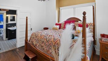 A four-poster bed with a patterned bedspread, a wooden nightstand, a bedside table, and a white feathered decorative piece.