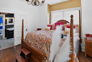 A four-poster bed with a patterned bedspread, a wooden nightstand, a bedside table, and a white feathered decorative piece.