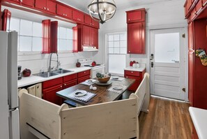 A kitchen with red cabinets, a wooden dining table, and a white refrigerator.