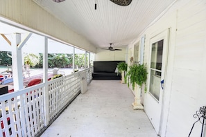 A covered porch with a white railing, a black sofa, and potted plants.