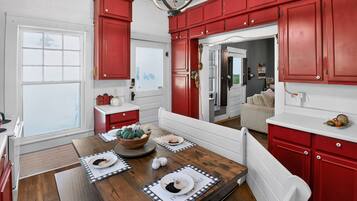 Une cuisine avec des meubles de rangement rouges, une table à manger en bois et une vue sur le salon.