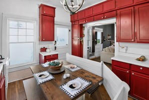 A kitchen with red cabinets, a wooden dining table, and a view into the living area. - Cozy Aberdeen MS Retreat Near Lake & MSU (Aberdeen)