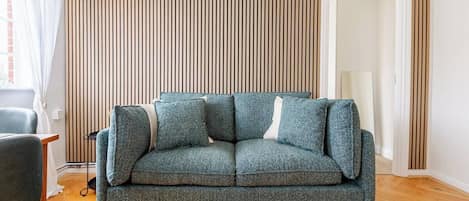 Una sala de estar con un sofá, una silla, un radiador y una puerta.