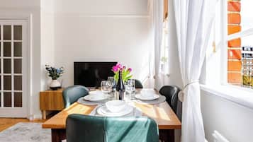 A dining area with a wooden table set for four, a TV on the wall, and a brick wall.