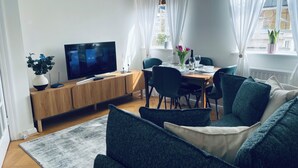 Una sala moderna con una televisión, una mesa de comedor para dos personas y un sofá con cojines.