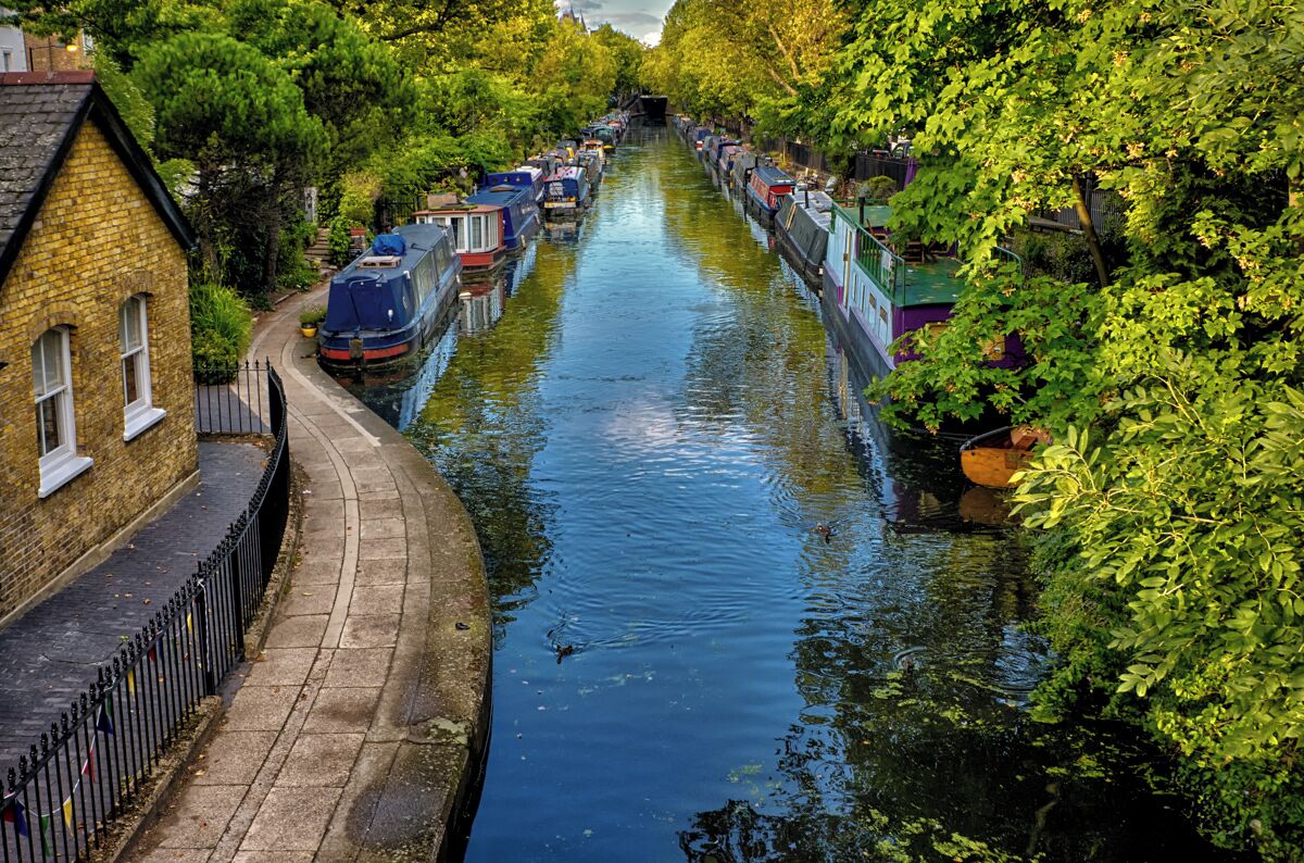 Un canal étroit où naviguent des bateaux, un bâtiment en briques et une promenade dallée.