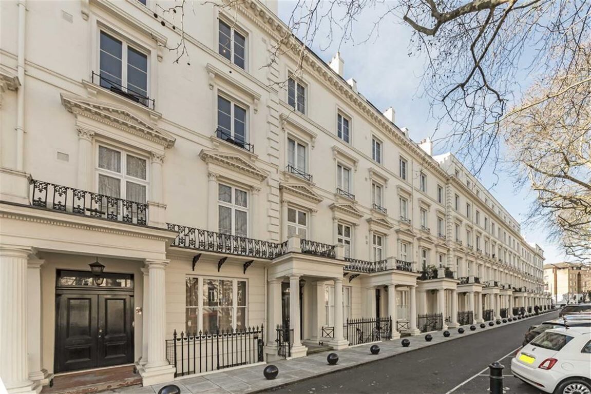 A row of classic, white, multi-story buildings with black railings and a clean, paved street.