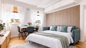 Un dormitorio moderno con cama, escritorio y silla, una ventana con cortinas y un panel de pared de madera.