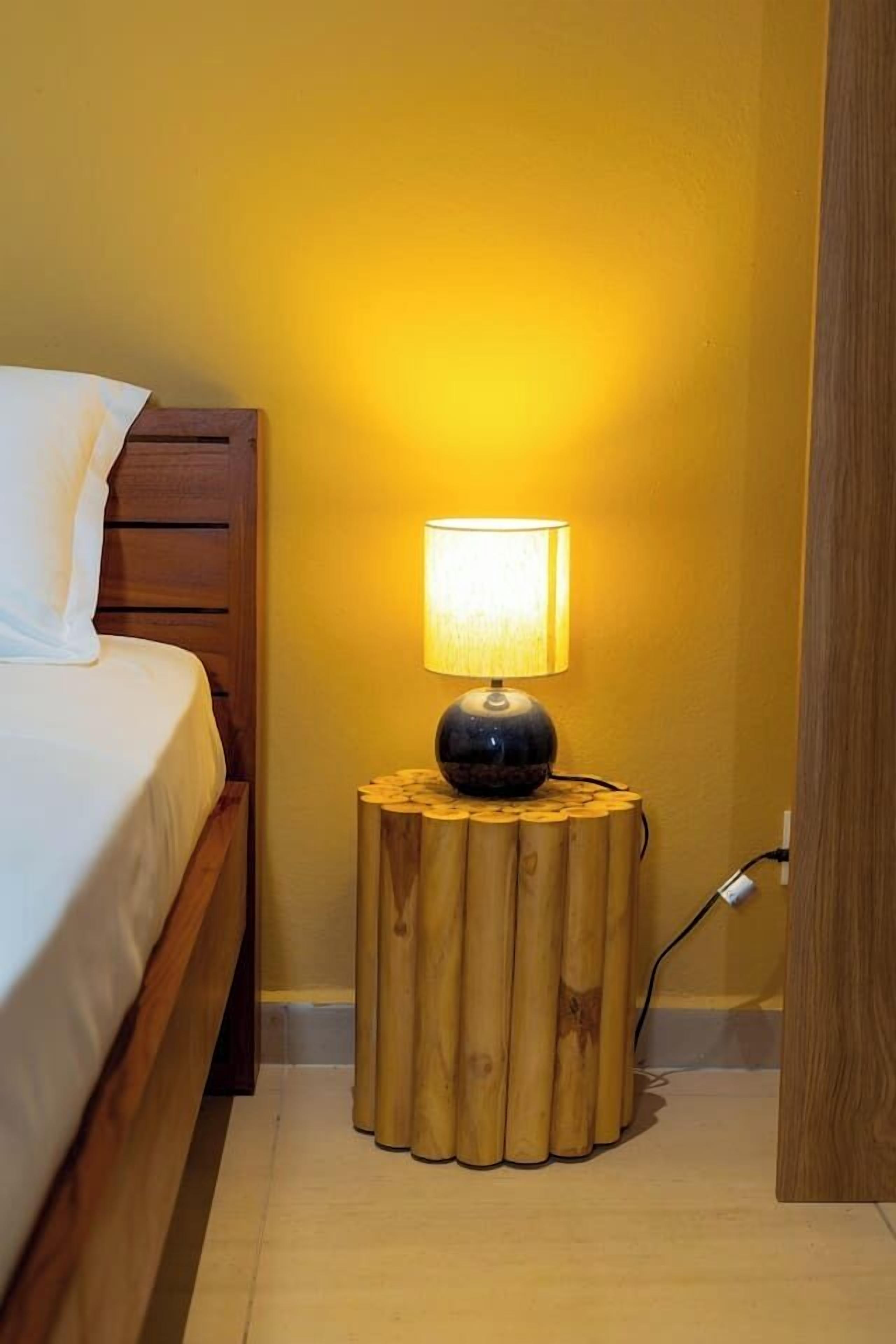 Ein Bett mit Holz-Kopfteil, eine Nachttischlampe auf einem Holzschemel und eine Steckdose.