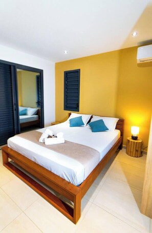 A hotel room with a bed, a bedside lamp, and a window with blinds. - Amazonia: Central, quiet three-bedroom apartment with a private pool (Les Abymes)
