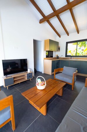 Ein modernes Wohnzimmer mit Fernseher, Holzmöbeln, einer Küchenzeile und einem Fenster mit Ausblick.