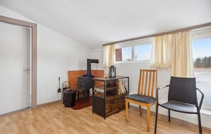 A room with a fireplace, a wooden chair, a small table, and a window with curtains. - 2 bedroom nice apartment in Ringkøbing (Ringkøbing)