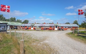 A red building with a gravel driveway, a small outdoor seating area, and a flagpole with a flag.