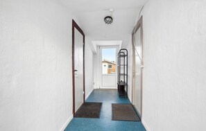 A narrow hallway with a blue floor, a white door at the end, and a black metal shelf on the right wall. - 2 bedroom nice apartment in Ringkøbing (Ringkøbing)
