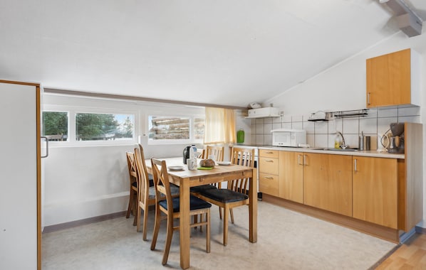 A compact kitchen with wooden cabinets, a dining table with chairs, and a view through the window.