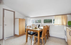 A compact kitchen with a dining table, chairs, a refrigerator, and a window with curtains.