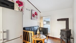 A cozy living area with a sofa, a small wooden table with a bottle and glass, a black stove, and artwork on the walls. - Stunning apartment in Ringkøbing with WiFi (Ringkøbing)