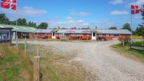 A row of red-roofed buildings with outdoor seating, a gravel path, and two flags. - Stunning apartment in Ringkøbing with WiFi (Ringkøbing)