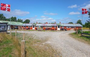 A building with a gravel driveway, outdoor seating area, and a flagpole. - Cozy home in Ringkøbing with WiFi (Ringkøbing)