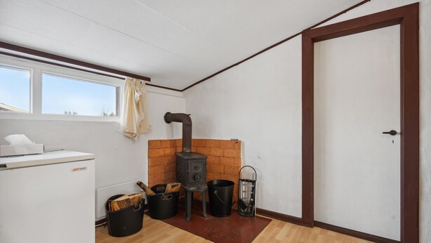 A compact kitchen with a wood-burning stove, a refrigerator, and a window with curtains. - Cozy home in Ringkøbing with WiFi (Ringkøbing)