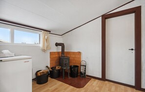 A compact kitchen with a wood-burning stove, a refrigerator, and a window with curtains.