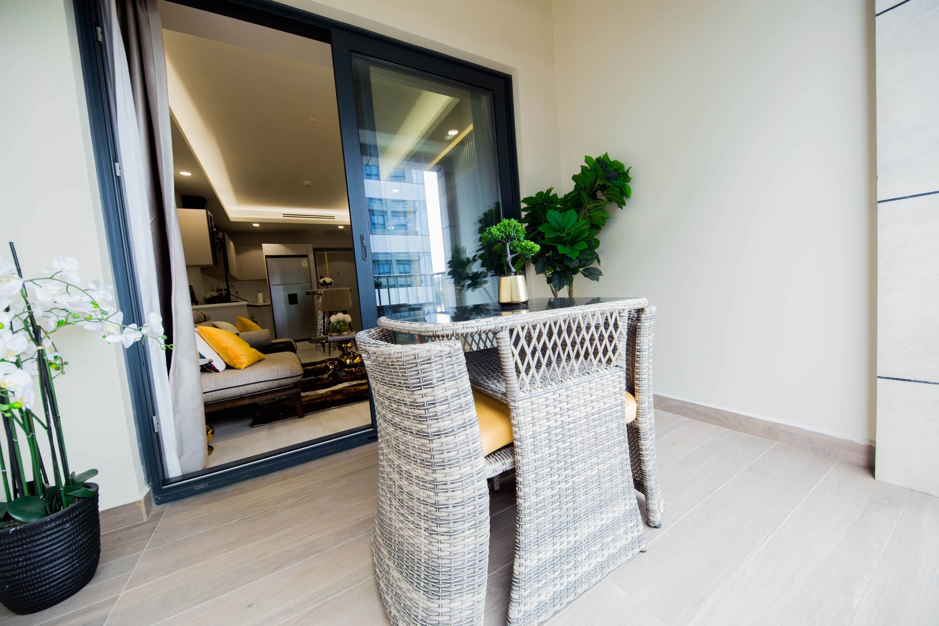 A modern living space with a glass door leading to a bedroom, a wicker chair, and a small table with a plant.