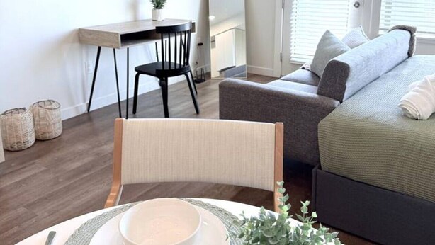 Ett modernt och väl upplyst rum med en säng, ett skrivbord, en stol och en matplats med ett bord dukat för två personer.