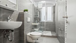 A modern bathroom with a white sink, toilet, and shower area. - Apartmenthaus VINA -  Smart Urban Stay (Kassel)