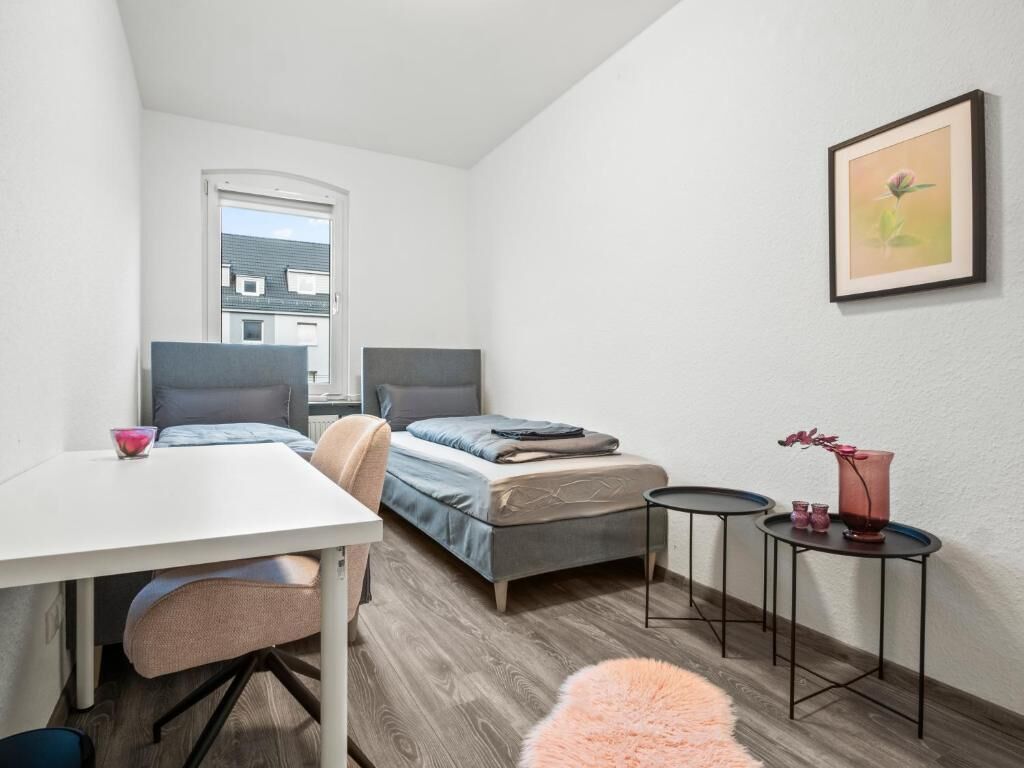 A compact room with a bed, a desk, a chair, a small table, and a window.
