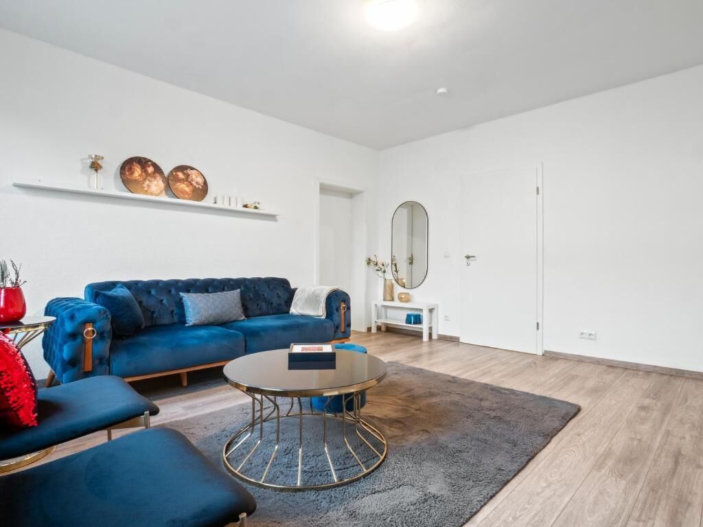 Una sala de estar moderna con un sofá azul, una mesa de centro redonda y un espejo en la pared.