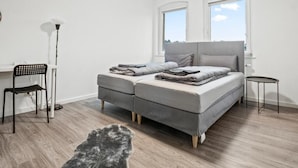 A bedroom with a bed, a chair, a small table, and a floor lamp. - Apartmenthaus VINA -  Smart Urban Stay (Kassel)