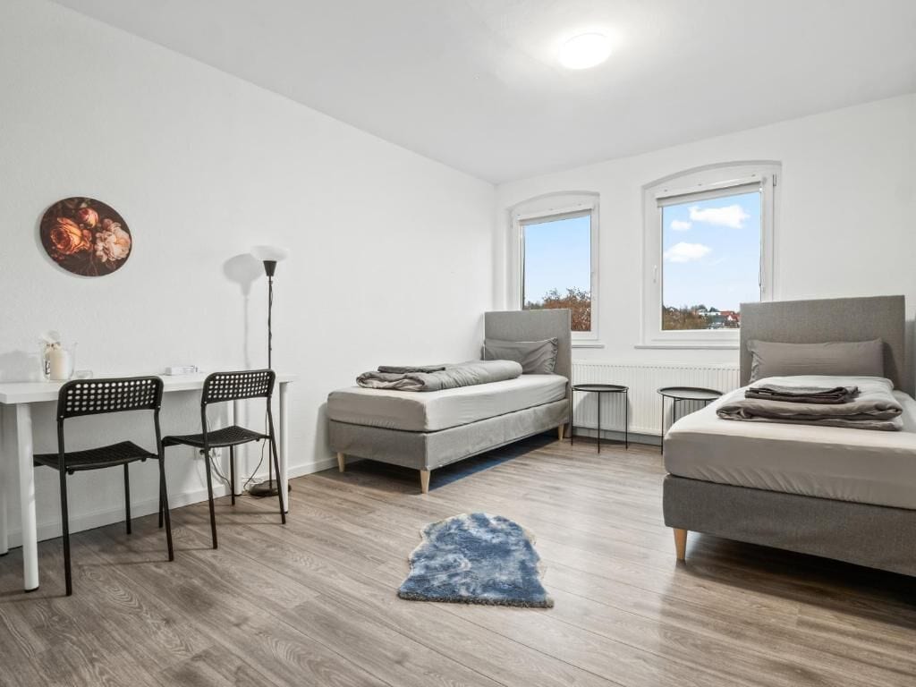 Ein modernes Schlafzimmer mit Schreibtisch, zwei Stühlen, einem Bett und einem Fenster.