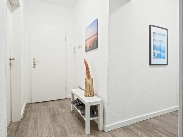 A hallway with a white door, a bench with a vase, and two framed pictures on the wall. - Apartmenthaus VINA - Smart Urban Stay (Kassel)