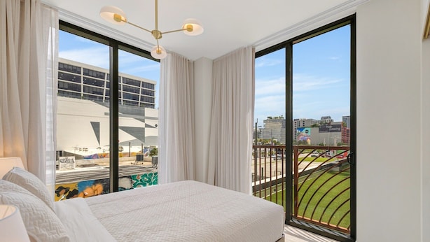Un dormitorio con una cama grande, vistas a un paisaje urbano y un balcón con barandilla.