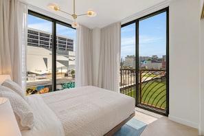 A bedroom with a large bed, a view of a cityscape, and a balcony with a railing. - Miami Oasis 2BR Apartment with Pool (Miami)