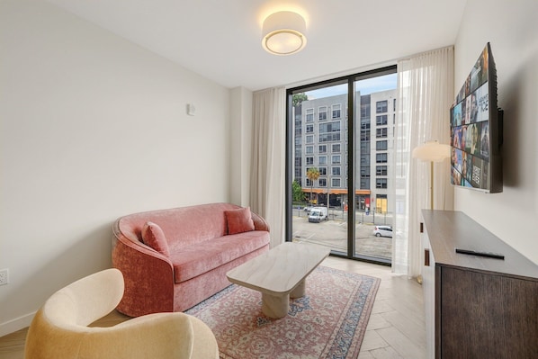 A modern living room with a red sofa, a beige armchair, a wooden coffee table, and a TV mounted on the wall. - Miami Oasis 2BR Apartment with Pool (Miami)