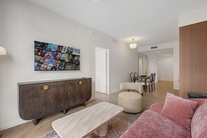 A modern living room with a dark wood console, a beige sofa, a coffee table, and a wall-mounted movie poster. - Miami Oasis 2BR Apartment with Pool (Miami)