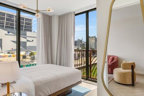 A modern hotel room with a large bed, a balcony with a city view, a round mirror, and a red chair. - Miami Oasis 2BR Apartment with Pool (Miami)